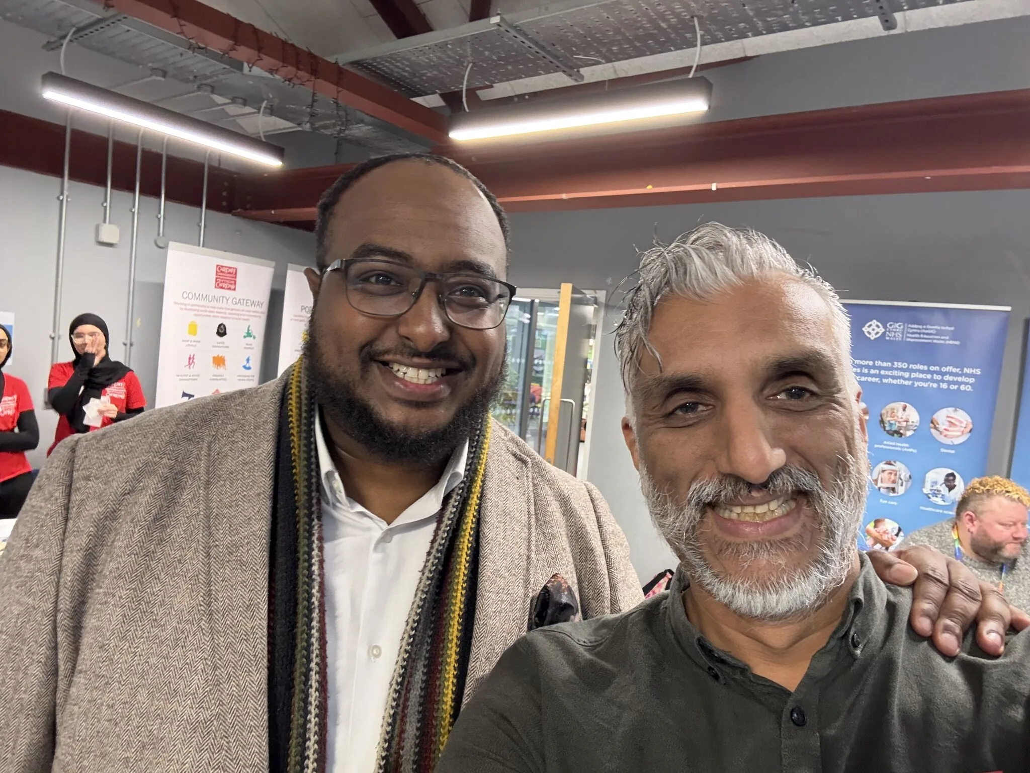 Dr Sarju and a colleague at a community health careers event, with Community Gateway and NHS Wales banners behind them.