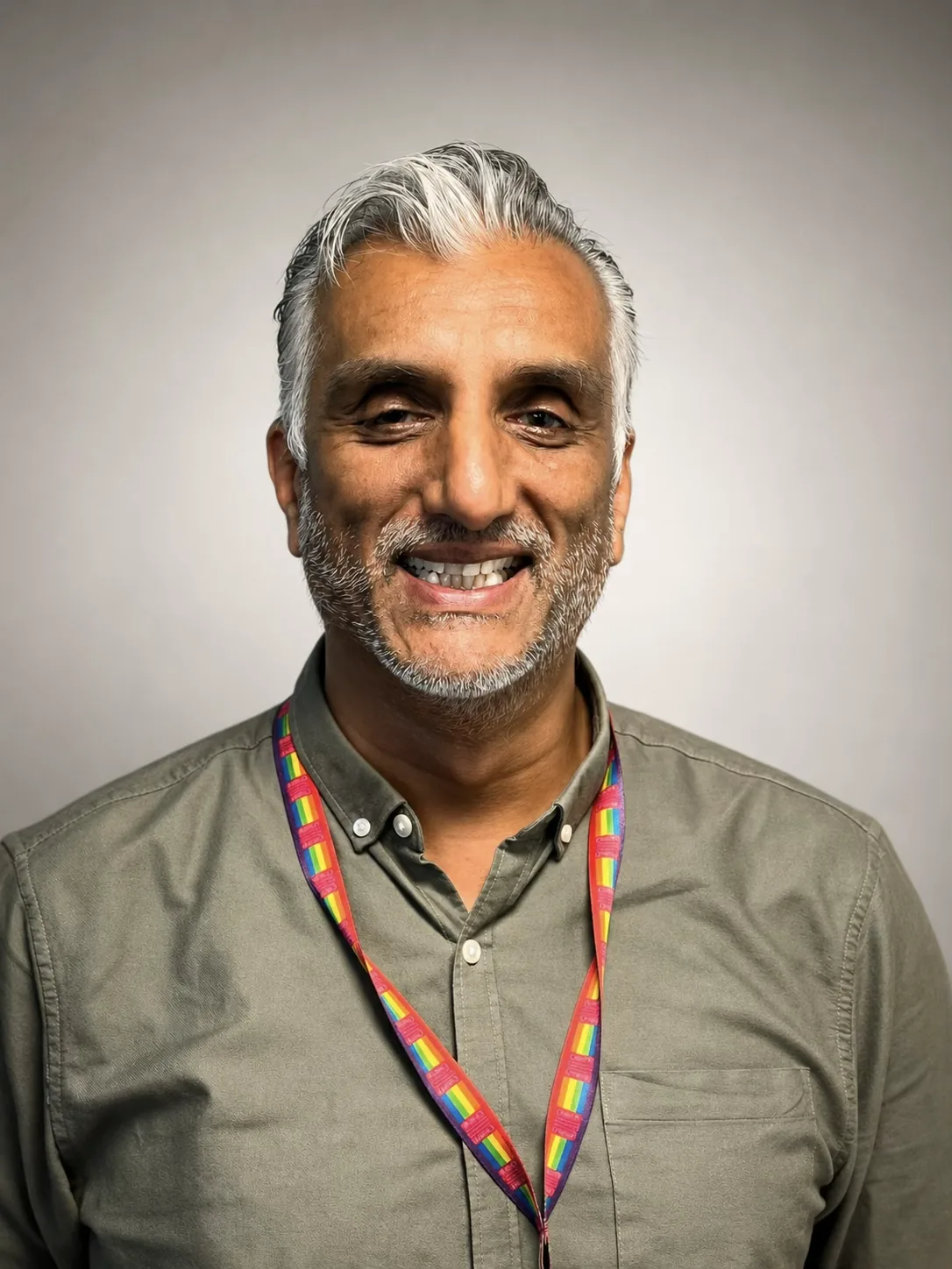 Dr Sarju smiling to camera in a studio portrait, in an olive shirt with a rainbow lanyard round his neck.