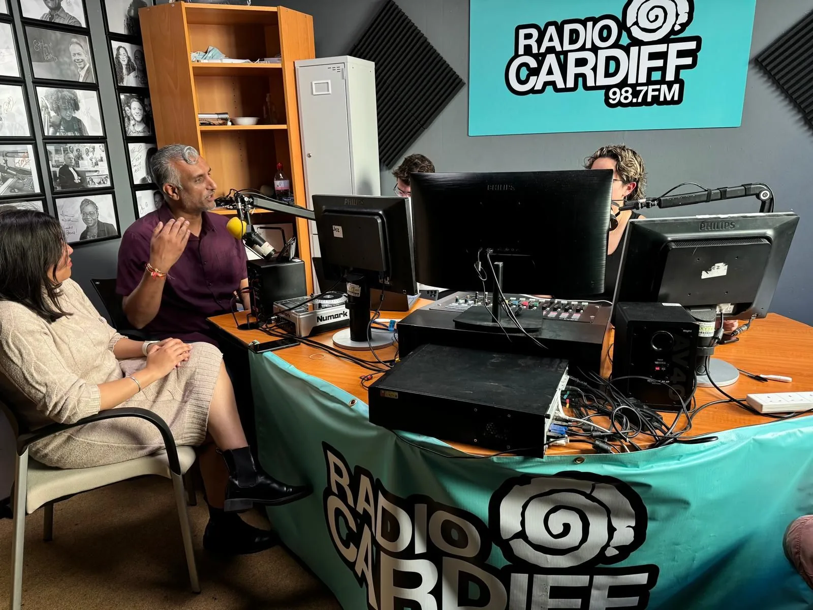 Dr Sarju mid-sentence at a microphone in the Radio Cardiff 98.7FM studio, with two others at the desk.