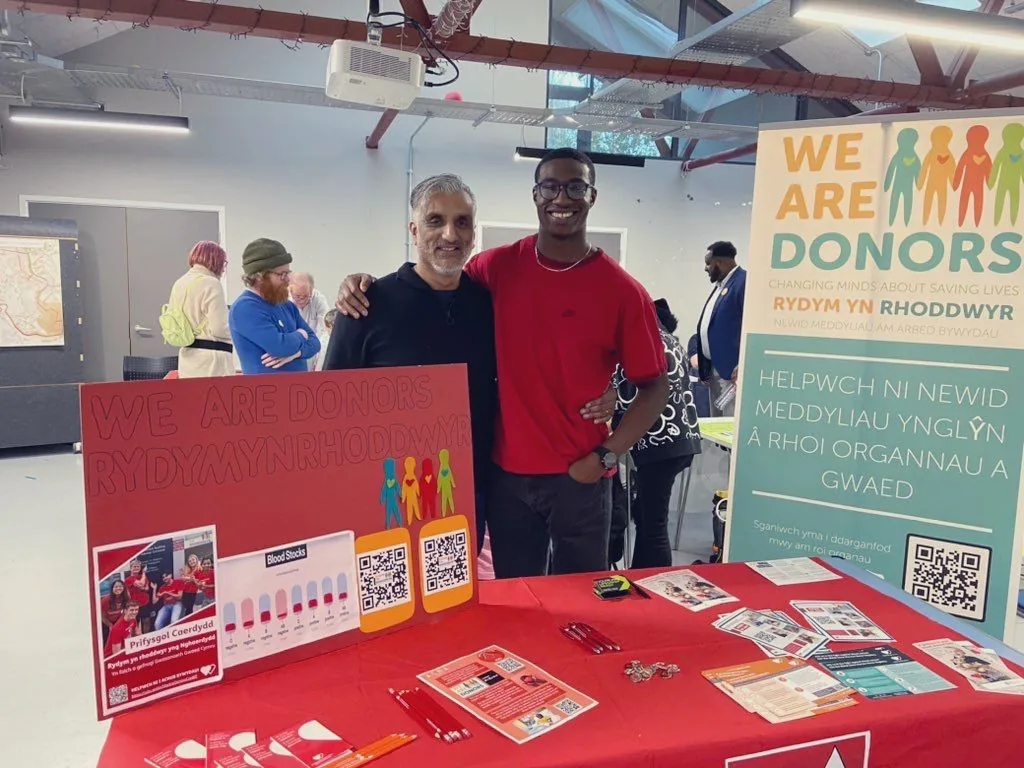 Dr Sarju with a student behind the We Are Donors stand, a bilingual organ and blood donation campaign, with leaflets and a QR code display on the table.